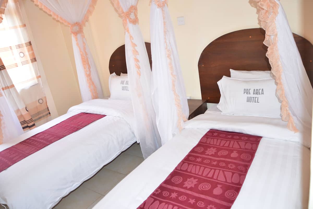 A hotel room with two beds, each with a canopy and pillows labeled "PRE AREA HOTEL".