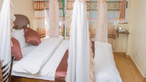 Een kamer met een bed onder een witte hemel, een houten stoel en een kleine tafel met een telefoon.
