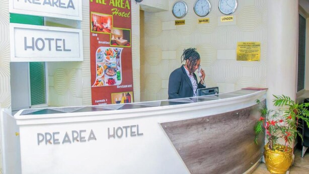 Een receptiebalie van een hotel met een bord waarop 'PRE AREA HOTEL' staat en een poster die ontbijt en restaurantdiensten promoot.