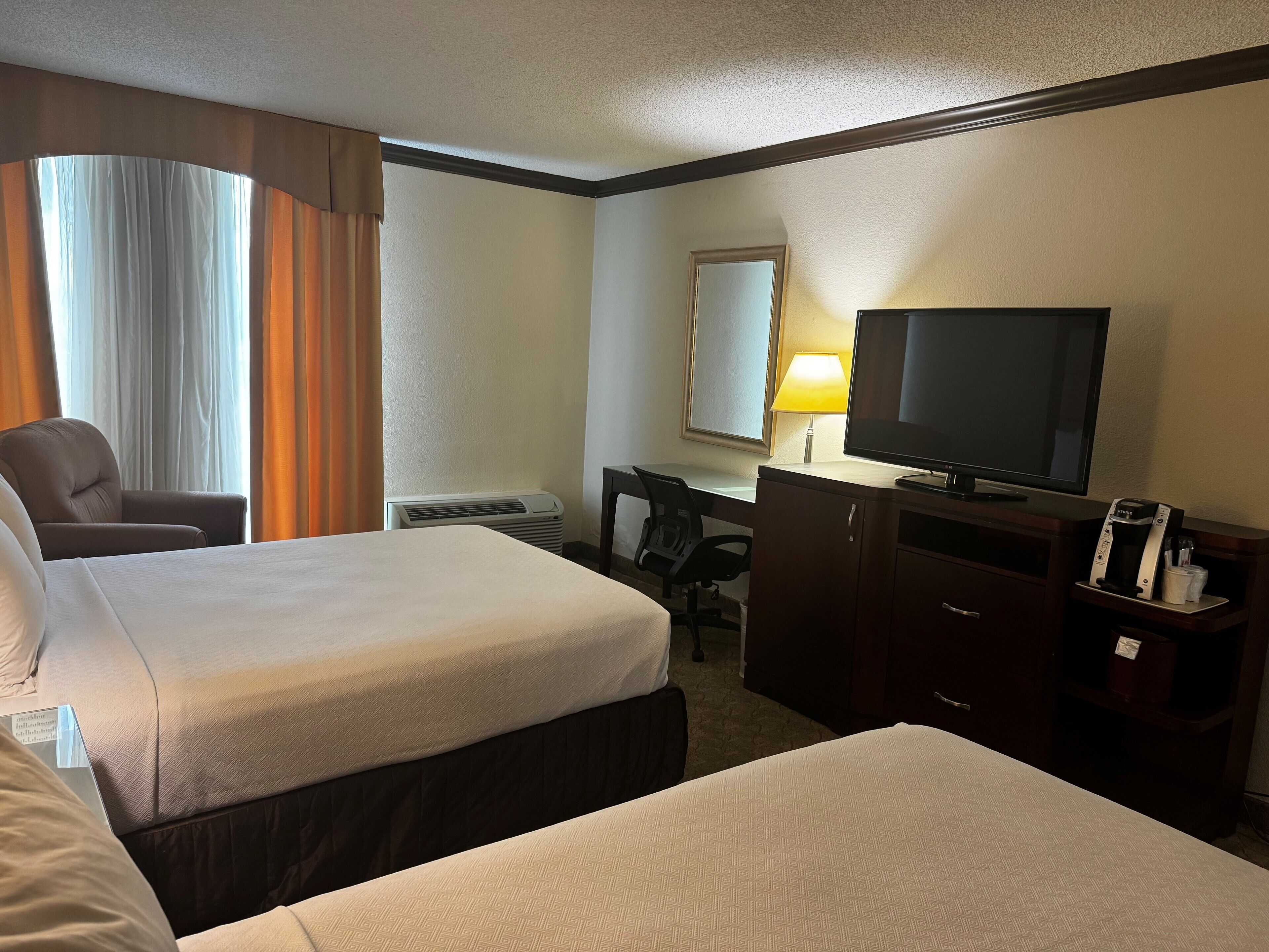 A hotel room with two beds, a desk with a chair, a television, and a coffee maker.
