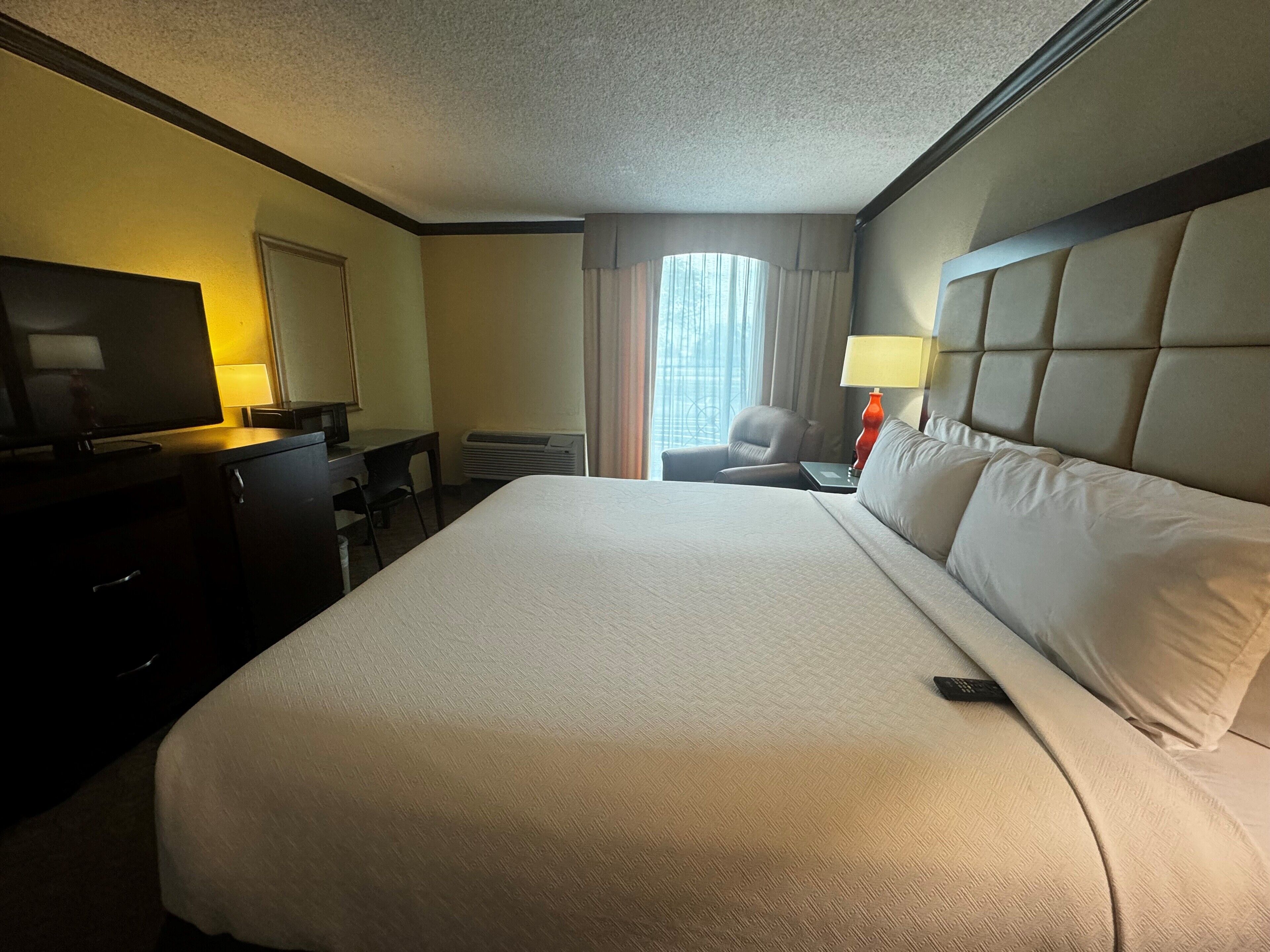 Een hotelkamer met een groot bed, een bureau met televisie, een stoel en een raam met gordijnen.