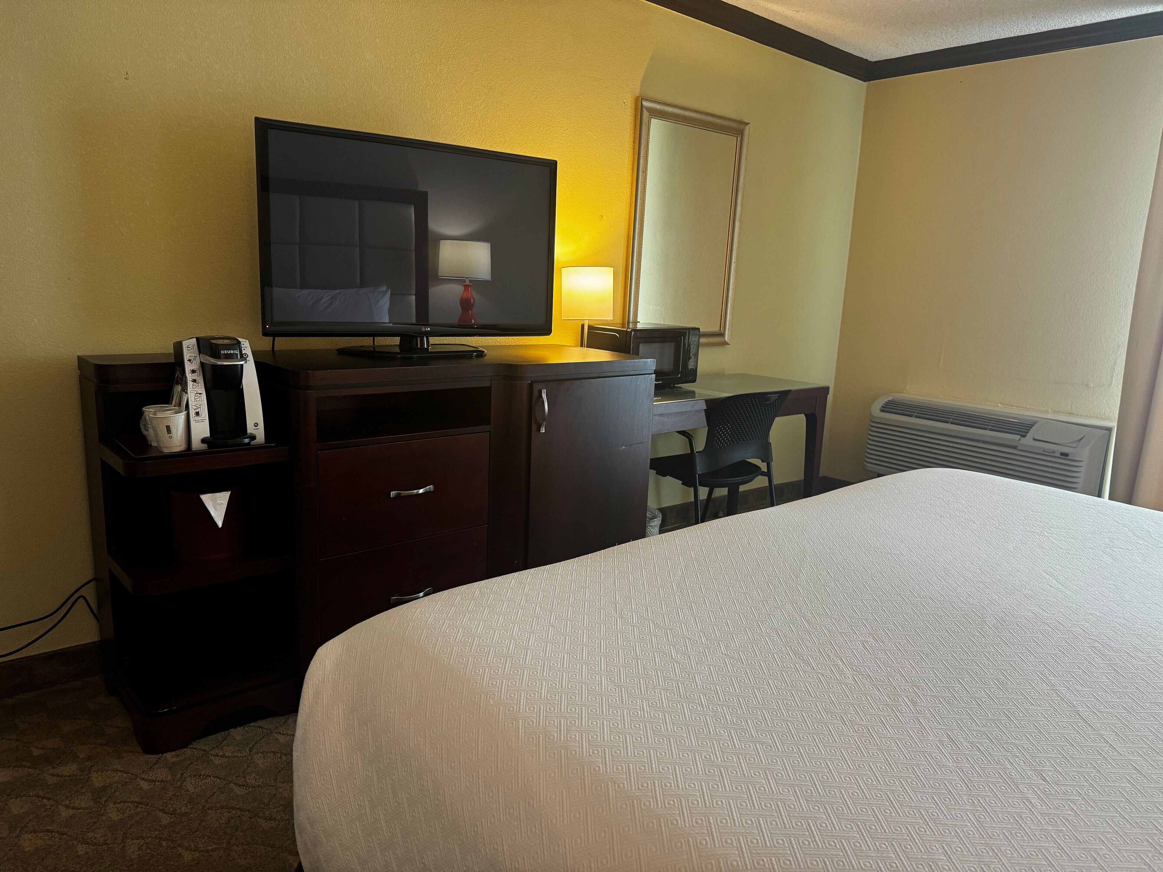 A hotel room with a bed, a desk with a computer, a television, a coffee maker, and a mirror.