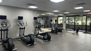 A gym with various exercise equipment, including treadmills and weight machines, and a large window providing a view of the outside. - Wingate Houston at Reliant Park & Medical Center (Houston)