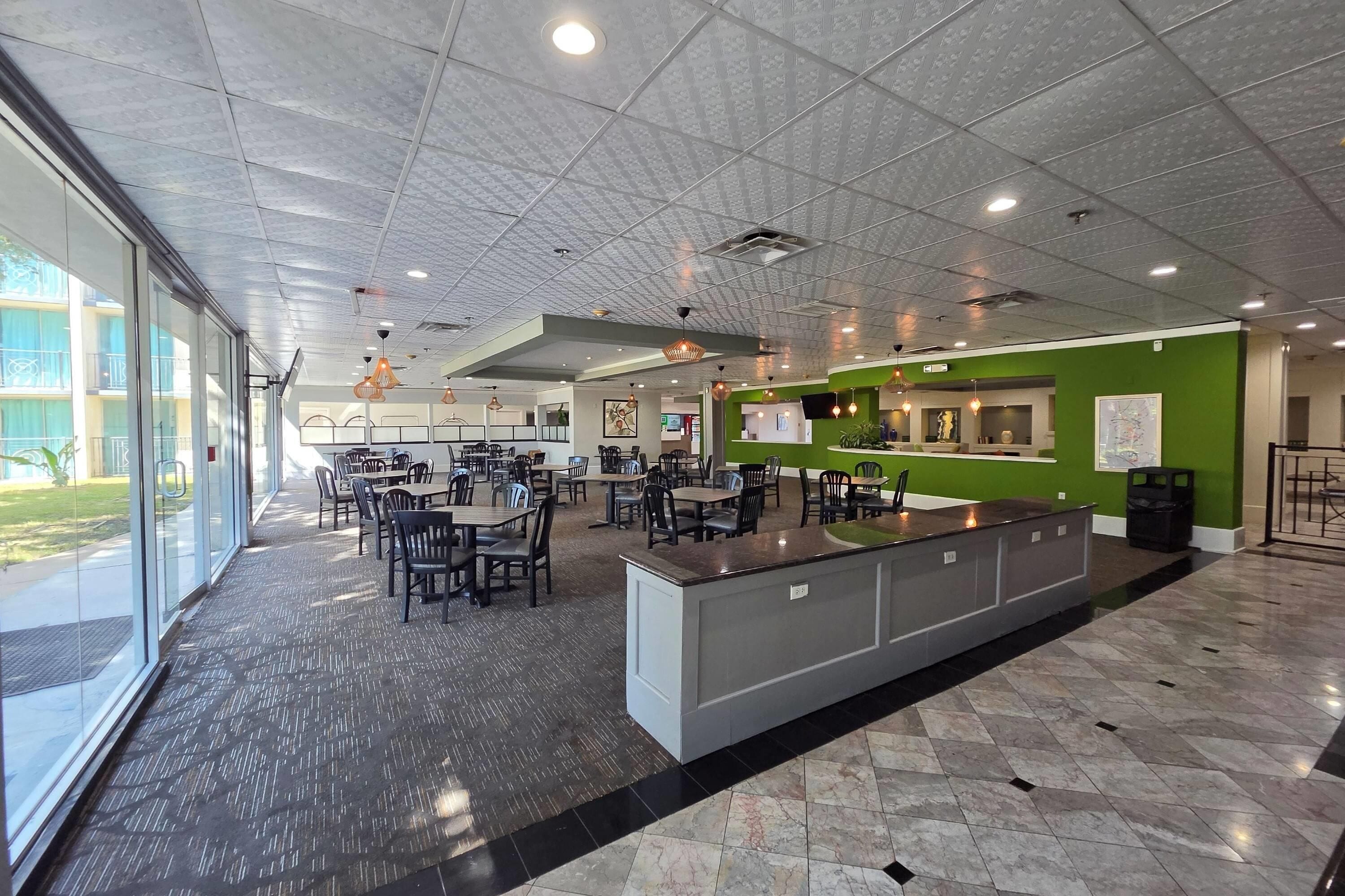 A spacious indoor area with multiple tables and chairs, a reception desk, and a large window providing natural light.