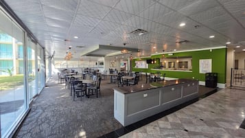 A spacious indoor area with multiple tables and chairs, a reception desk, and a large window providing natural light.