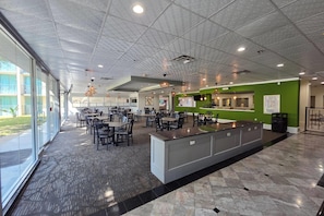 A spacious indoor area with multiple tables and chairs, a reception desk, and a large window providing natural light. - Wingate Houston near Reliant Park/Medical Center (Houston)