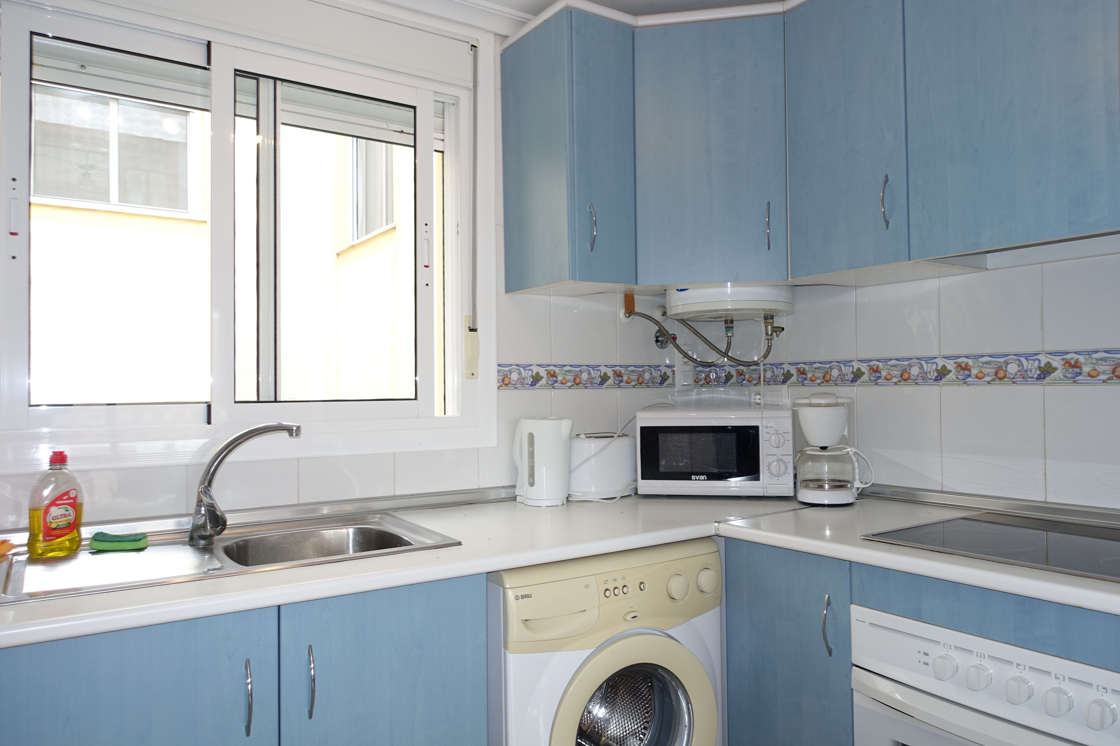 Une cuisine avec des meubles de rangement bleus, un lave-linge, un four à micro-ondes et une machine à café.
