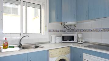 Une cuisine avec des meubles de rangement bleus, un lave-linge, un four à micro-ondes et une machine à café.