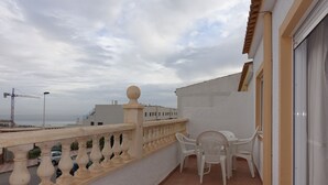 A balcony with a white railing, a table with chairs, and a view of the sea and construction cranes in the background. - 3 Bed first floor Apartment, communal pool and sea views, wifi. (Gran Alacant)
