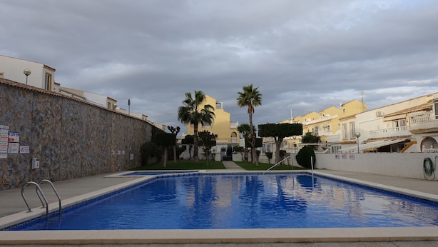 A swimming pool with a stone wall and palm trees. - 3 Bed first floor Apartment, communal pool and sea views, wifi. (Gran Alacant)