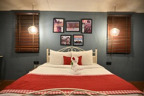 A neatly made bed with a red and white checkered bedspread, a white pillow, and a white towel with a red flower. There are framed posters on the wall above the bed, and two pendant lights hanging above. - Woodstock Resort (Shillong)