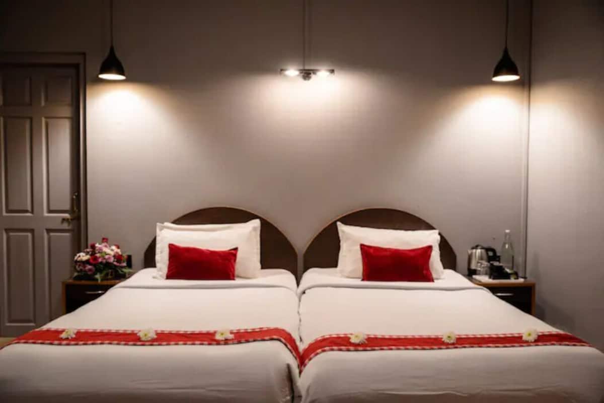 A double bed with a red and white bedspread, two bedside tables with lamps, and a door in the background.