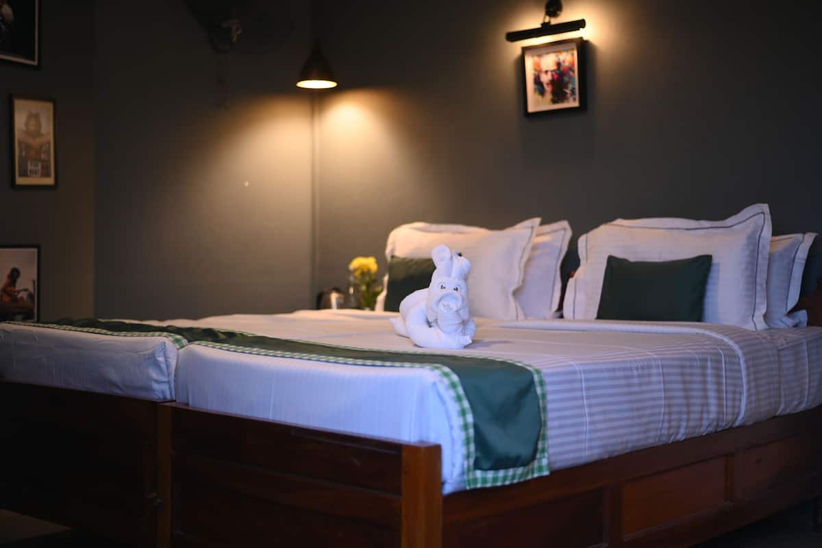 A neatly made bed with white linens, a green checkered throw, and a white towel shaped like an elephant.