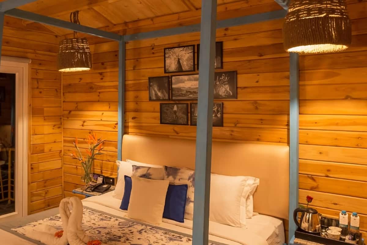 A wooden cabin interior with a four-poster bed, a dining area with a table and chairs, and a window with a view.