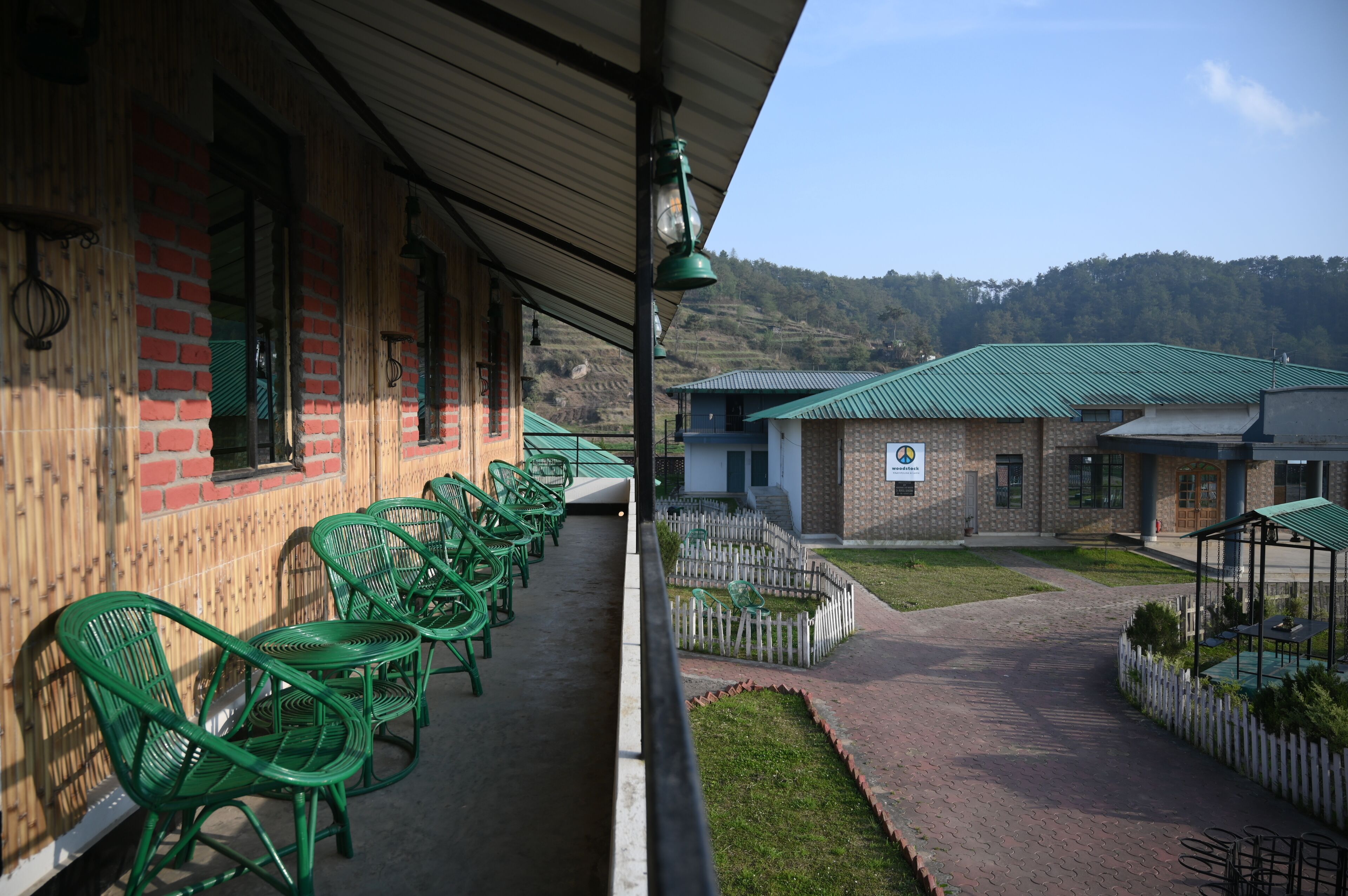 Un edificio con fachada de ladrillo, sillas verdes dispuestas en el exterior y un sendero que conduce a otro edificio con techo verde.