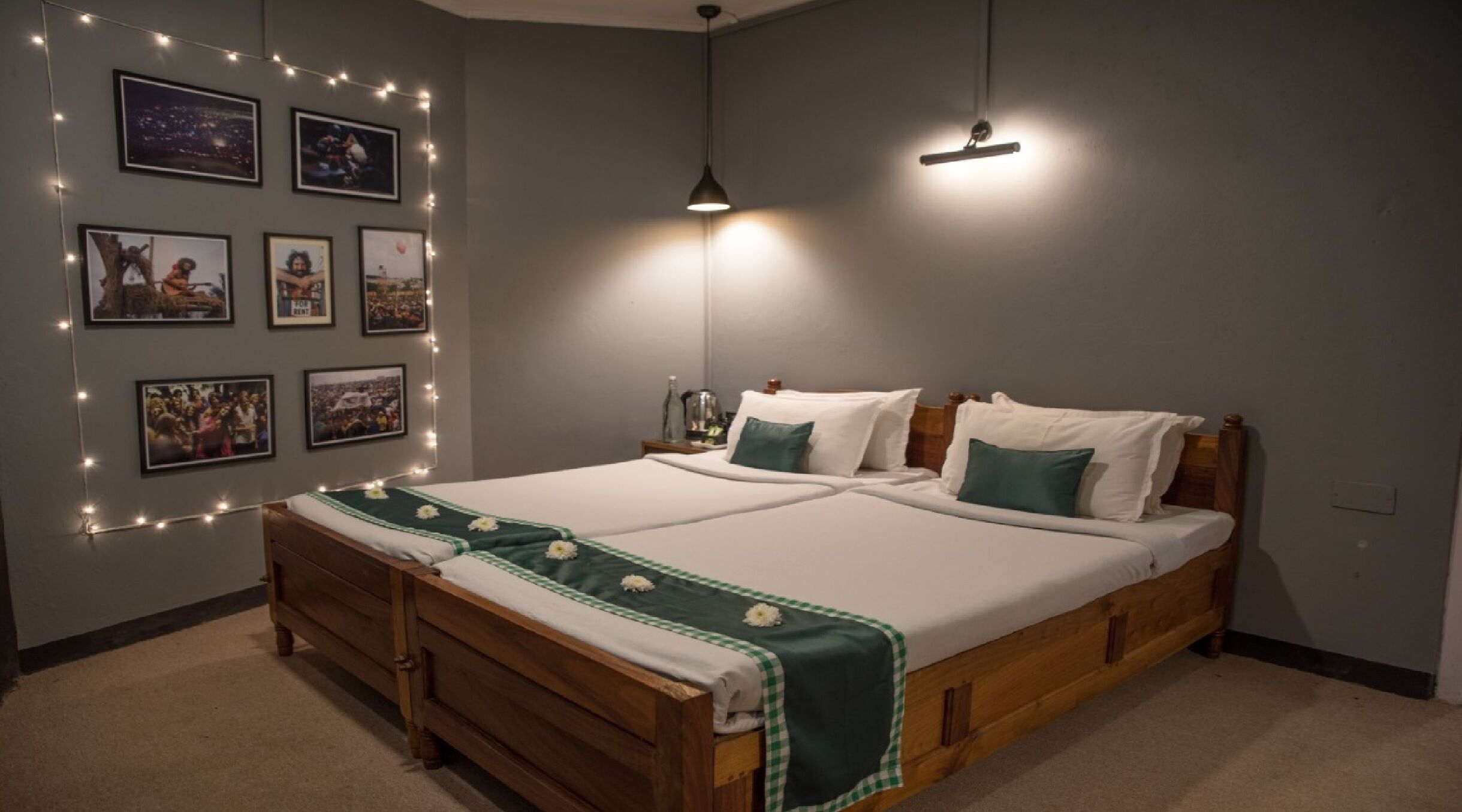 A double bed with a wooden frame, two pillows, a green and white checkered blanket, and string lights on the wall.
