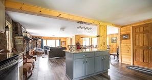 Amplia sala de estar con isla de cocina, chimenea de piedra y paredes de madera.