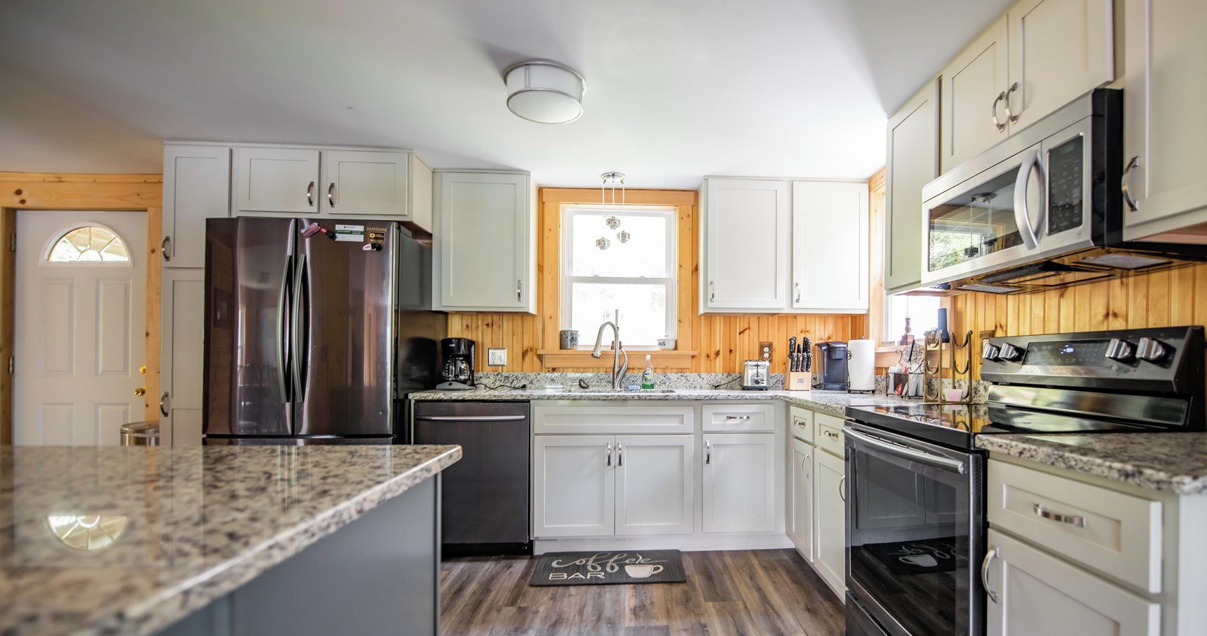 A kitchen with white cabinets, stainless steel appliances, a granite countertop, and a wooden floor.