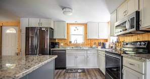 Una cocina con armarios blancos, electrodomésticos de acero inoxidable, encimera de granito y suelo de madera.