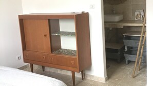 Een slaapkamer met een bed, een houten kledingkast, een badkamer met een wastafel en spiegel, en een ladder.