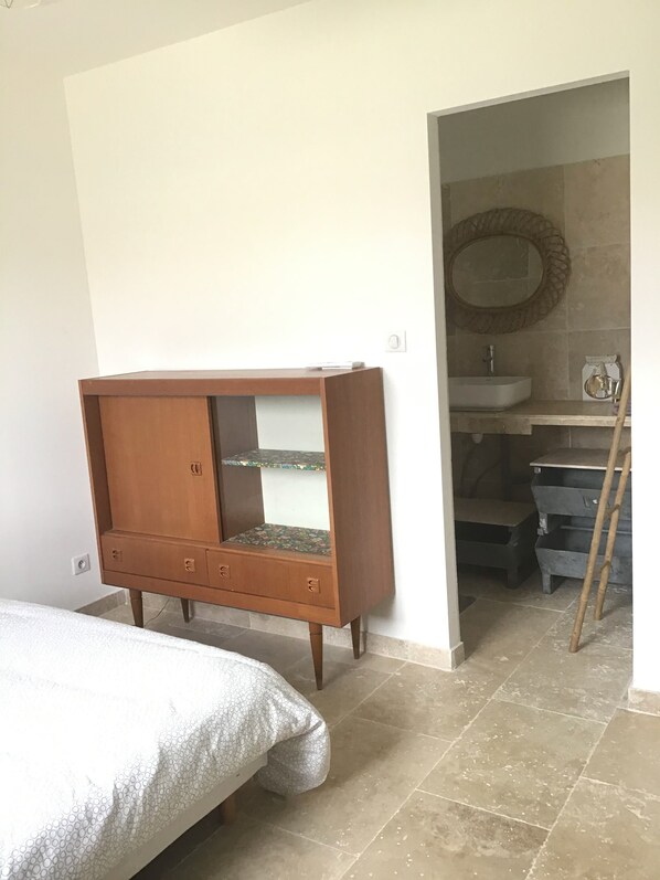 A bedroom with a bed, a wooden wardrobe, a bathroom with a sink and mirror, and a ladder.