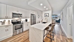A modern kitchen with white cabinets, stainless steel appliances, and a marble island. - Loggerhead Cay 274: Beautiful Condo on the Beach! (Sanibel)
