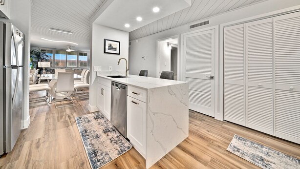 A modern kitchen with white cabinetry, a marble countertop, and a built-in dishwasher. - Loggerhead Cay 274: Beautiful Condo on the Beach! (Sanibel)