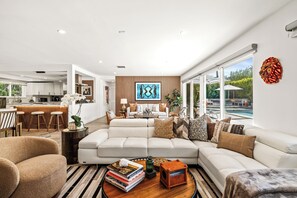 A modern living room with a sectional sofa, a coffee table with books, and a view of the outdoor pool area.