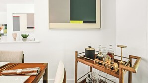Ein modernes Interieur mit minimalistischem Design, mit einem Holzes Esstisch, einem Metall-Beistelltisch mit Gläsern und einem großen abstrakten Gemälde an der Wand.