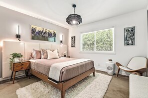 A modern bedroom with a large bed, bedside tables, a hanging light fixture, and artwork on the walls.