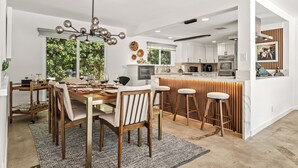 Una cucina moderna con mobili bianchi, un'isola centrale con sgabelli e un'area pranzo con tavolo e sedie in legno.