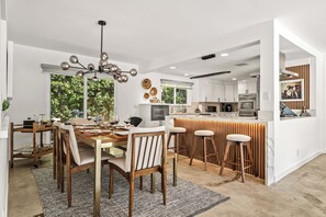 Une cuisine moderne avec des meubles blancs, un îlot central doté de tabourets et un coin repas avec une table et des chaises en bois.