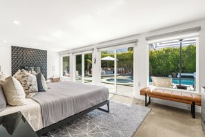 A bedroom with a large bed, a bench, and a view of a pool through the glass doors.