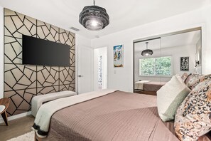Un dormitorio moderno con una cama grande, un televisor de pantalla plana montado en una pared con diseño geométrico, un espejo grande y una lámpara en el techo.