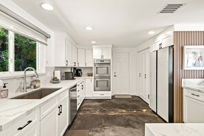 Een moderne keuken met witte kasten, roestvrijstalen apparatuur en een marmeren aanrecht.