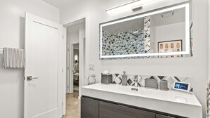 Un bagno moderno con un mobile lavabo bianco, un grande specchio e uno schienale geometrico.