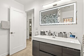 Une salle de bain moderne avec un meuble-lavabo blanc, un grand miroir et un revêtement mural à motifs géométriques.