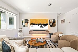Una sala de estar moderna con un televisor grande de pared, una mesa redonda con libros y un sofá.