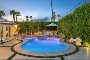 Une piscine au design incurvé, entourée d’une pelouse bien entretenue et d’une haie.
