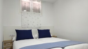 Ein Schlafzimmer mit einem Bett, zwei Kissen, einem Nachttisch und einem Fenster mit Vorhängen.