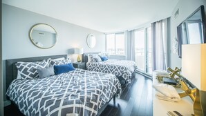 A hotel room with two beds, a large window, and a bedside table with a lamp.
