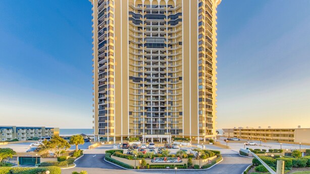 A tall, multi-story hotel with a central courtyard and a view of the sea.