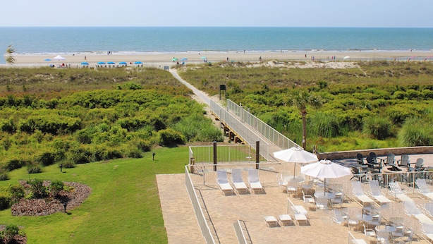 Ein Strandhotel mit Terrasse, Sitzgelegenheiten und Sonnenschirmen, einem Weg zum Strand und Blick aufs Meer.