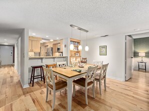 A modern kitchen with wooden cabinets, a dining area with a wooden table and chairs, and a hallway with a door leading to another room.