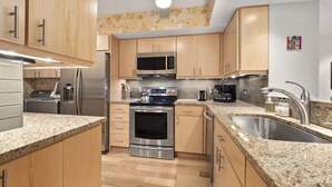Eine moderne Küche mit Holzausstattung, Edelstahlgeräten, Granit-Arbeitsplatten und einem eingebauten Backofen.