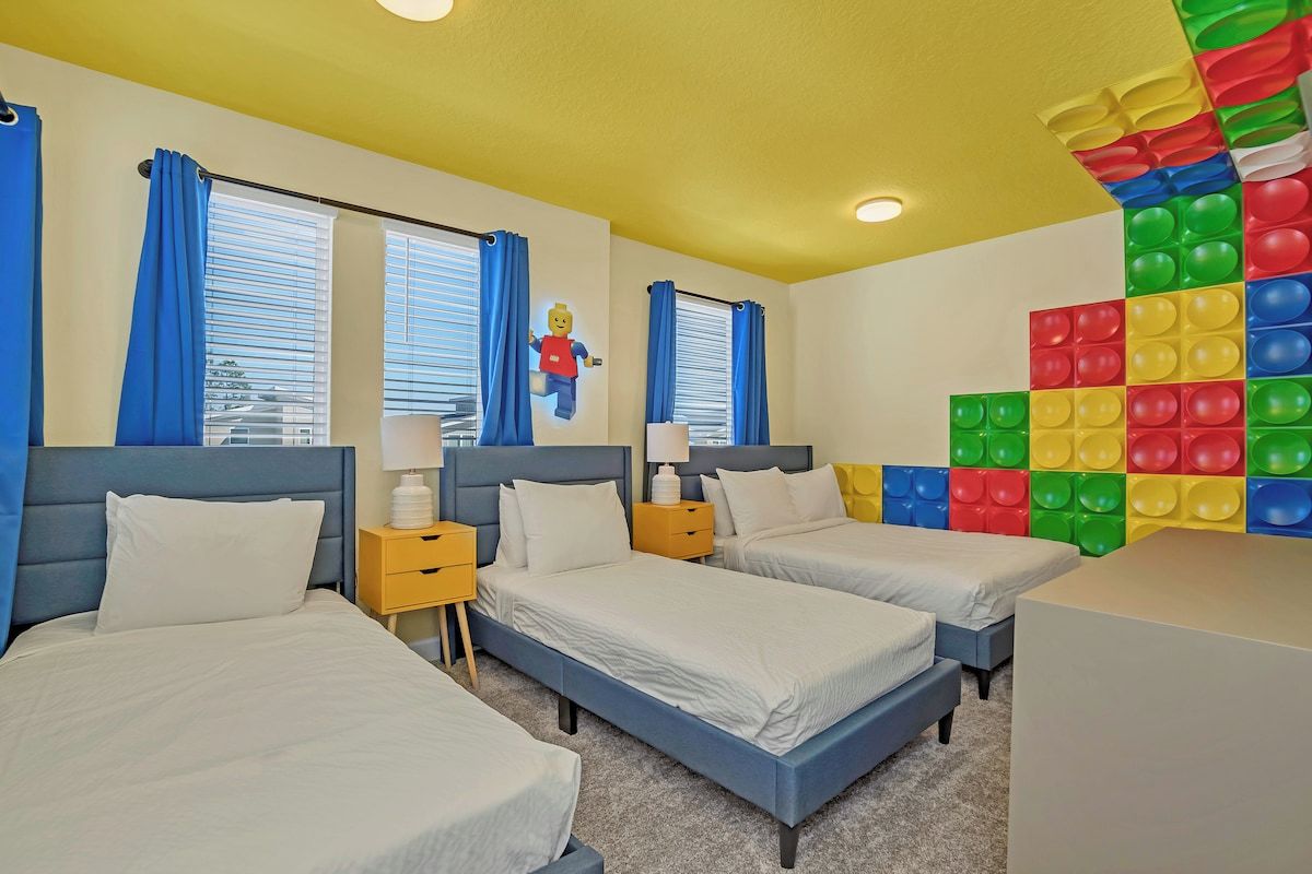 Une chambre d’hôtel avec deux lits, un mur décoré de couleurs vives et une fenêtre avec des rideaux bleus.