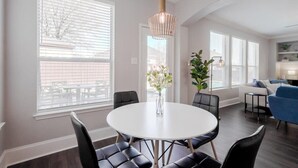A modern dining area with a round table, black chairs, and a hanging light fixture.