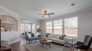 A spacious living room with a sofa, chairs, and a coffee table. There is a kitchen area visible in the background.