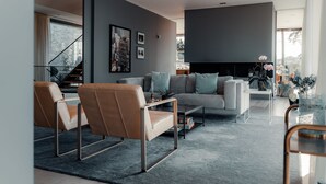 A modern living room with a sofa, armchairs, and a coffee table. There is a fireplace and a staircase in the background. - Most Luxurious 5-bed Villa in Boo Stockholm (Värmdö)