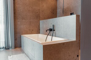 A modern bathroom with a large bathtub, tiled walls, and a visible shower area. - Most Luxurious 5-bed Villa in Boo Stockholm (Värmdö)